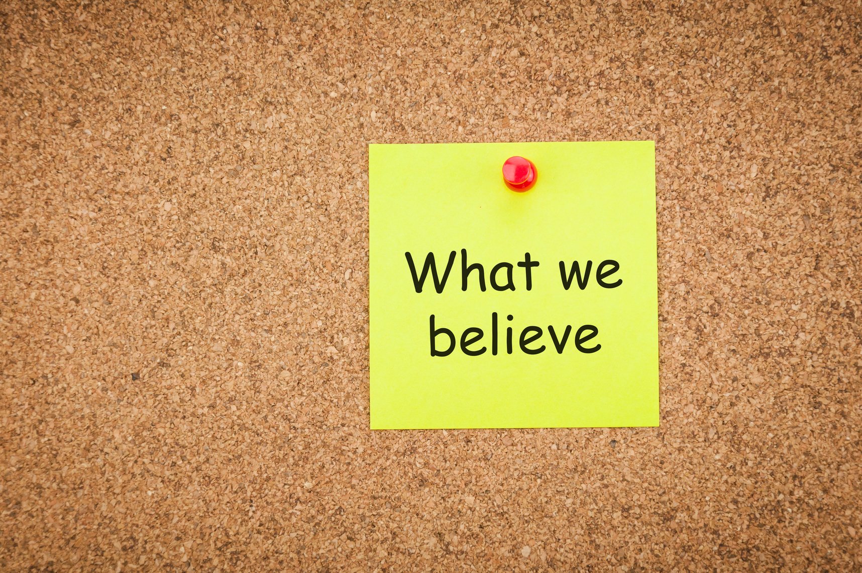 sticky note with word what we believe on corkboard